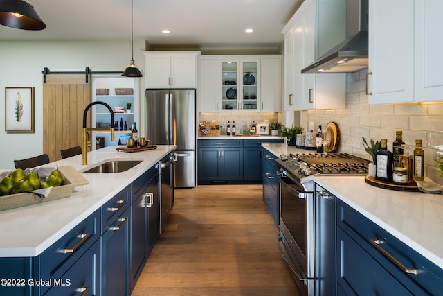 kitchen with wall chimney exhaust hood, stainless steel appliances, blue cabinetry, a barn door, and white cabinets