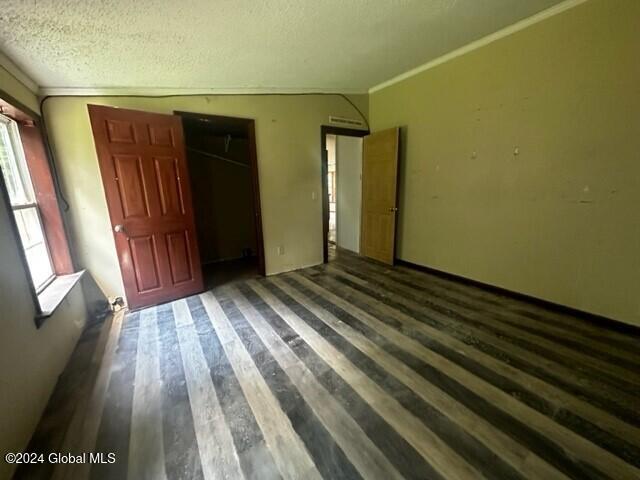 unfurnished bedroom with dark hardwood / wood-style flooring, crown molding, lofted ceiling, a textured ceiling, and a closet