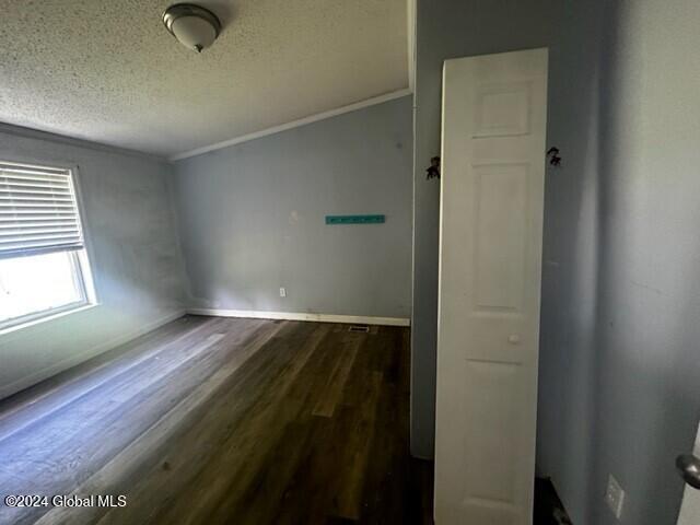 unfurnished room with a textured ceiling, vaulted ceiling, dark wood-type flooring, and crown molding