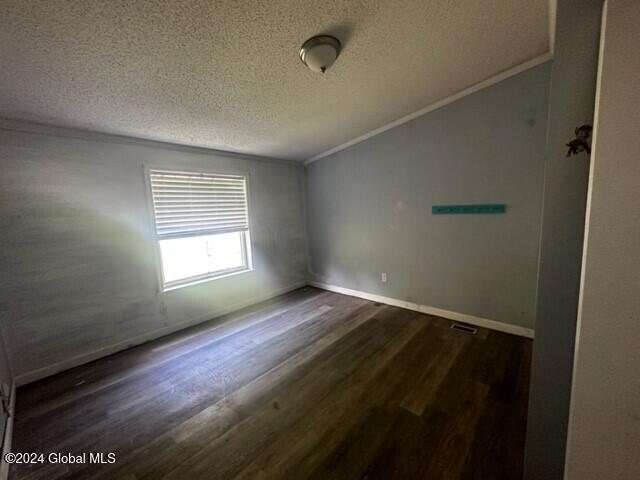 empty room with vaulted ceiling, crown molding, dark hardwood / wood-style flooring, and a textured ceiling