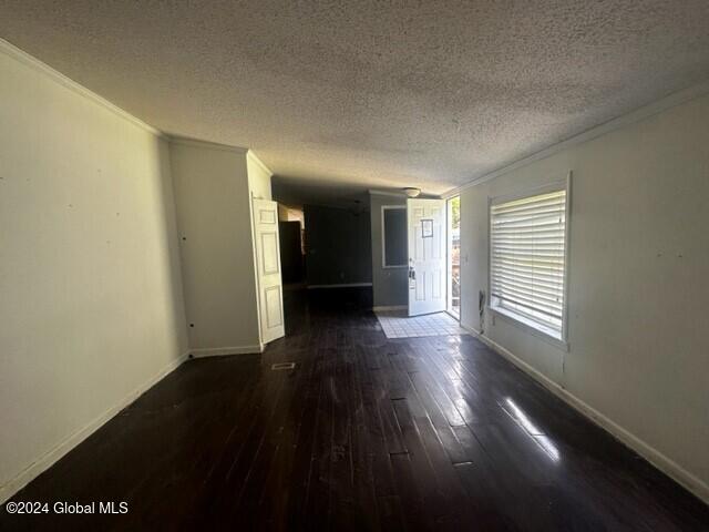 spare room with a textured ceiling, crown molding, and dark wood-type flooring