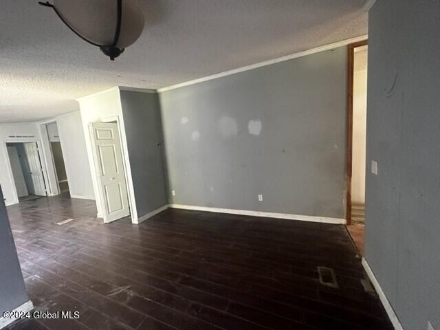 empty room featuring a textured ceiling, dark hardwood / wood-style floors, and crown molding