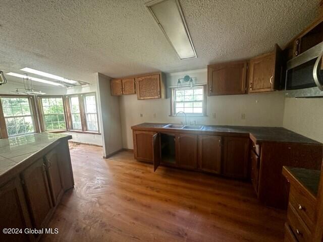 kitchen with a textured ceiling, tile counters, dark wood-type flooring, and sink