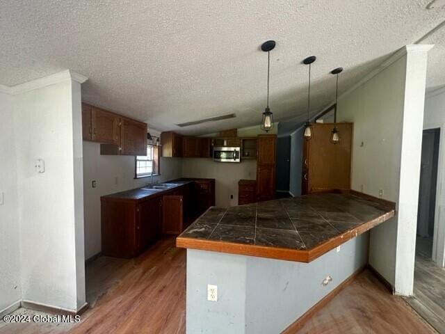 kitchen with hanging light fixtures, kitchen peninsula, hardwood / wood-style floors, a textured ceiling, and lofted ceiling