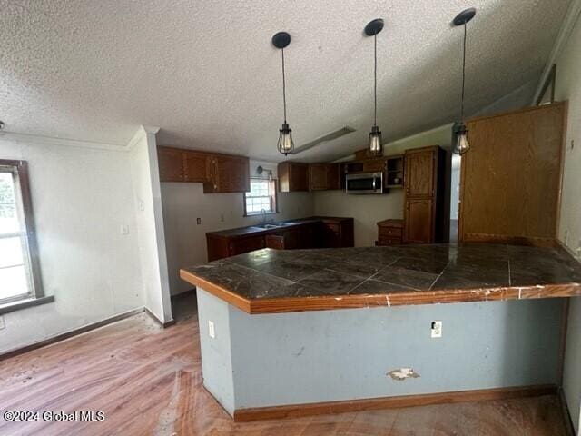 kitchen featuring kitchen peninsula, a textured ceiling, light hardwood / wood-style flooring, and vaulted ceiling