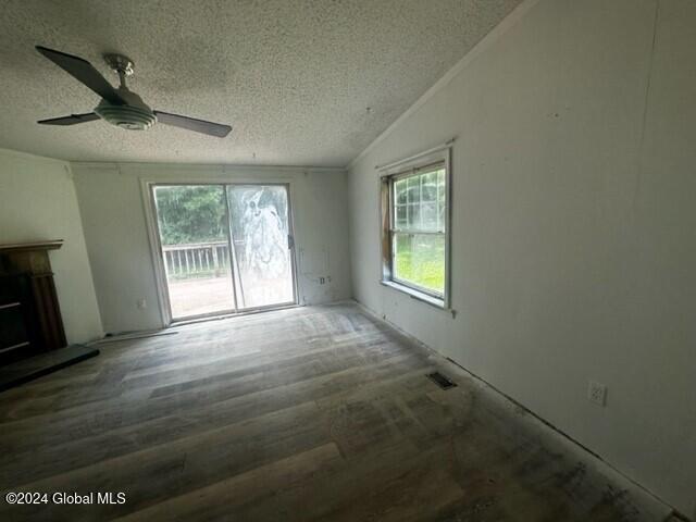 unfurnished living room with a textured ceiling, ceiling fan, vaulted ceiling, and hardwood / wood-style flooring