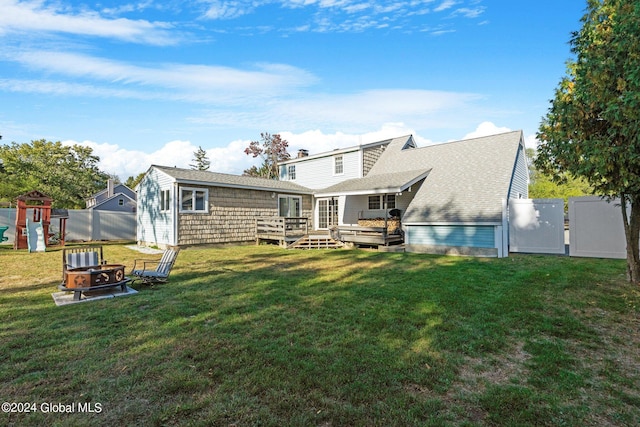 rear view of house featuring a lawn, a playground, a deck, and an outdoor fire pit