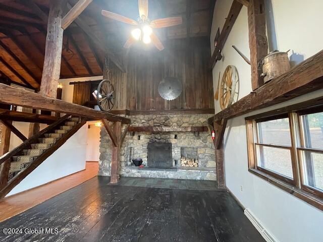 unfurnished living room with ceiling fan, lofted ceiling with beams, wooden ceiling, dark hardwood / wood-style floors, and a stone fireplace