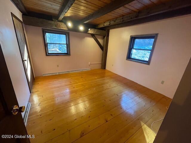 spare room featuring beamed ceiling, wooden ceiling, a baseboard heating unit, and light hardwood / wood-style floors