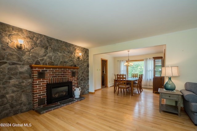 living room with a chandelier, a baseboard heating unit, a fireplace, and light hardwood / wood-style flooring