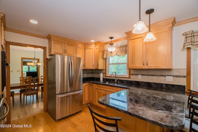 kitchen featuring stainless steel fridge, dark stone counters, sink, pendant lighting, and light hardwood / wood-style floors