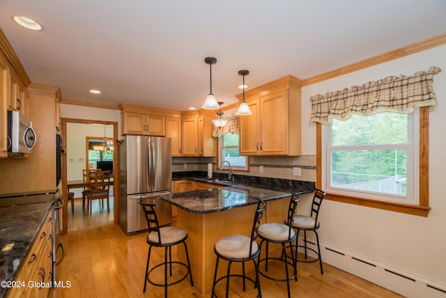 kitchen with hanging light fixtures, stainless steel appliances, dark stone counters, a breakfast bar area, and light wood-type flooring