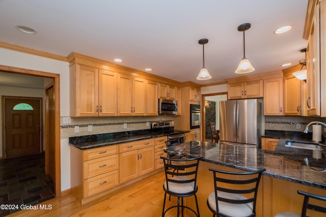 kitchen featuring sink, light hardwood / wood-style flooring, appliances with stainless steel finishes, decorative light fixtures, and a kitchen bar