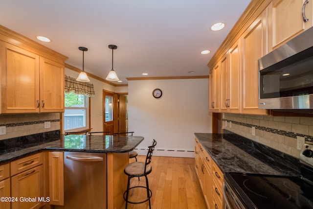 kitchen with dark stone countertops, ornamental molding, stainless steel appliances, and light wood-type flooring