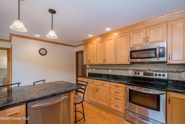 kitchen featuring tasteful backsplash, decorative light fixtures, a kitchen bar, appliances with stainless steel finishes, and light wood-type flooring