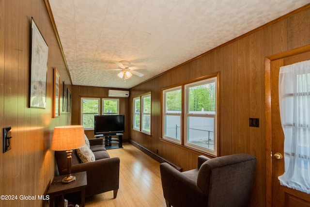 living room featuring ceiling fan, light hardwood / wood-style flooring, a wall unit AC, wood walls, and ornamental molding