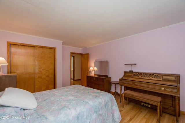 bedroom featuring light wood-type flooring, ornamental molding, and a closet