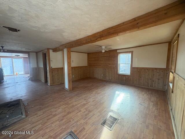 spare room featuring beam ceiling, ceiling fan, wooden walls, and light hardwood / wood-style floors