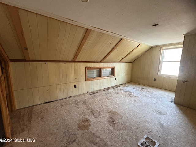 bonus room featuring a textured ceiling, lofted ceiling, and wood walls