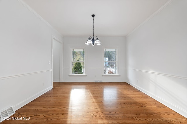 unfurnished dining area featuring hardwood / wood-style floors, ornamental molding, and a notable chandelier