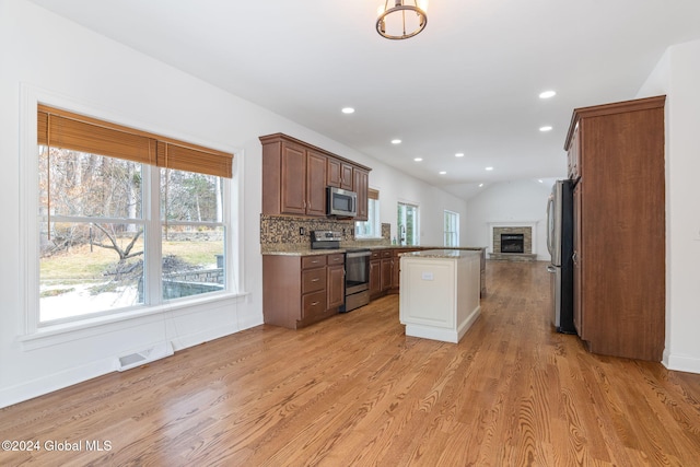 kitchen featuring stainless steel appliances, a stone fireplace, light stone counters, light hardwood / wood-style flooring, and backsplash