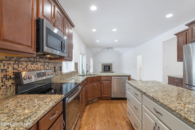 kitchen with light stone countertops, light wood-type flooring, backsplash, stainless steel appliances, and sink