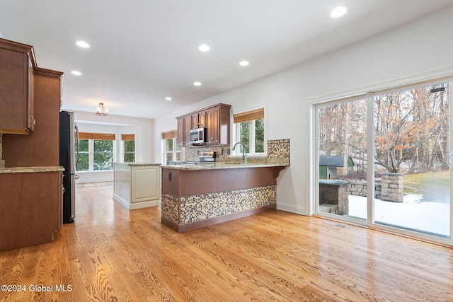 kitchen featuring backsplash, light hardwood / wood-style flooring, light stone countertops, kitchen peninsula, and stainless steel appliances