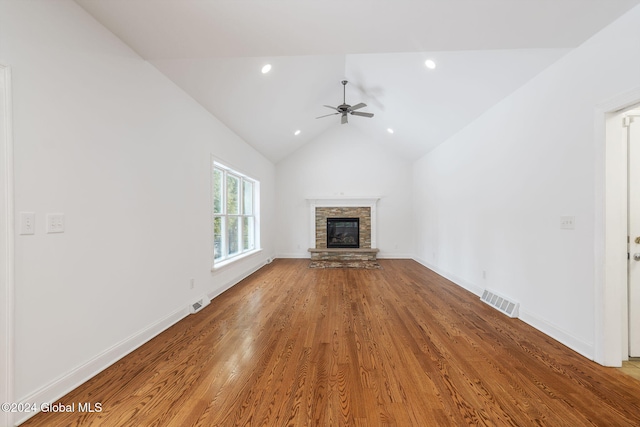 unfurnished living room featuring vaulted ceiling, hardwood / wood-style flooring, a stone fireplace, and ceiling fan