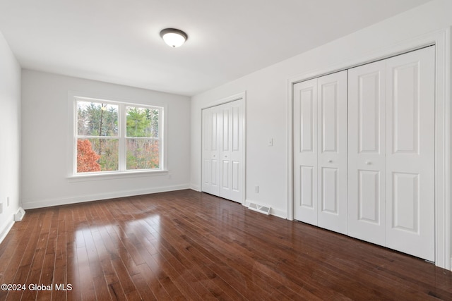 unfurnished bedroom with dark hardwood / wood-style floors and two closets