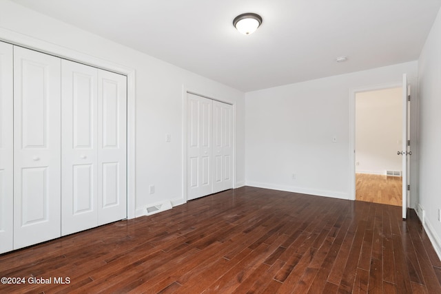 unfurnished bedroom with two closets and dark hardwood / wood-style floors