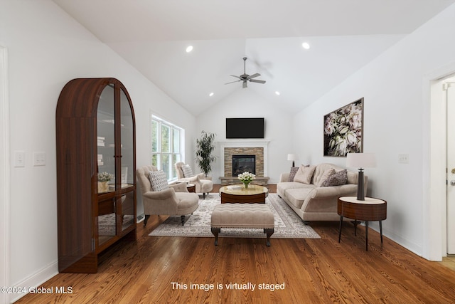 living room featuring hardwood / wood-style floors, ceiling fan, a stone fireplace, and vaulted ceiling