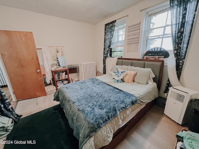 bedroom featuring a textured ceiling, wood-type flooring, and radiator heating unit