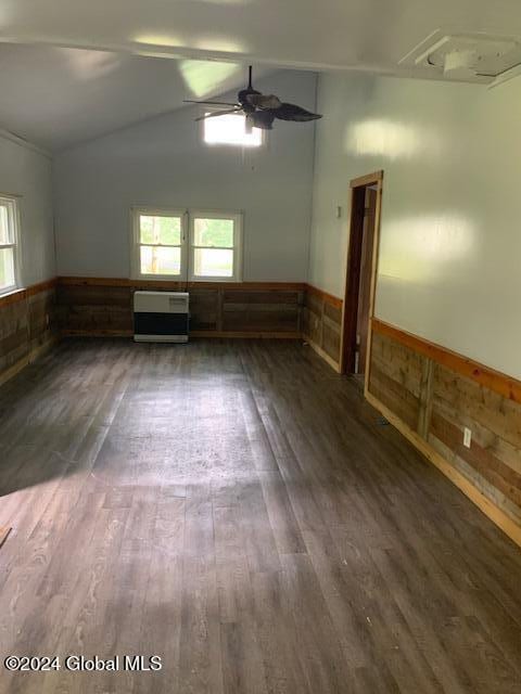 spare room with dark wood-type flooring, wooden walls, vaulted ceiling, ceiling fan, and heating unit