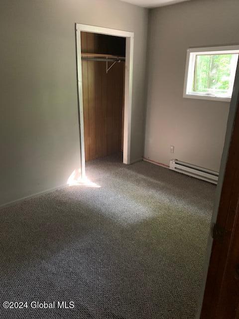 unfurnished bedroom with carpet, a baseboard radiator, and a closet