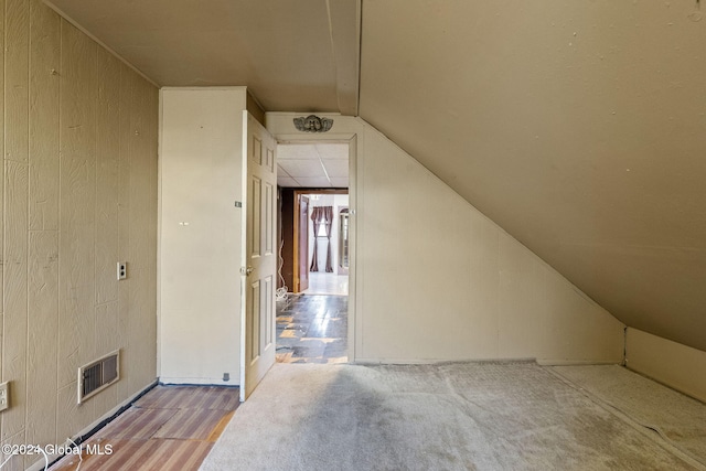 bonus room featuring vaulted ceiling and wood walls