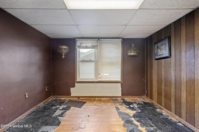 unfurnished room featuring wood-type flooring, a paneled ceiling, and wood walls