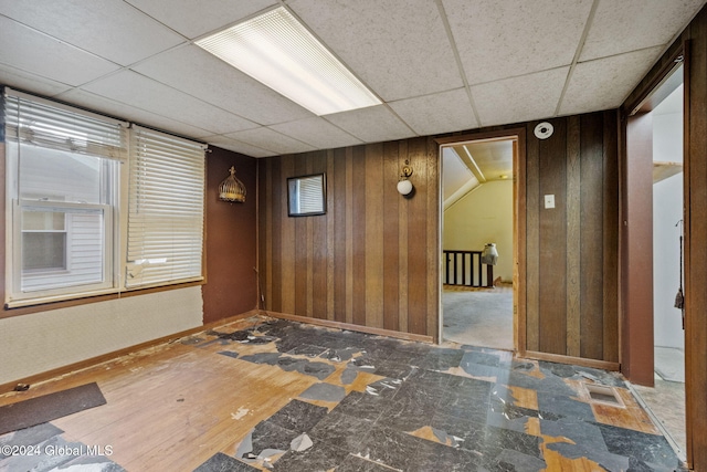 empty room featuring hardwood / wood-style floors, a paneled ceiling, wood walls, and a healthy amount of sunlight