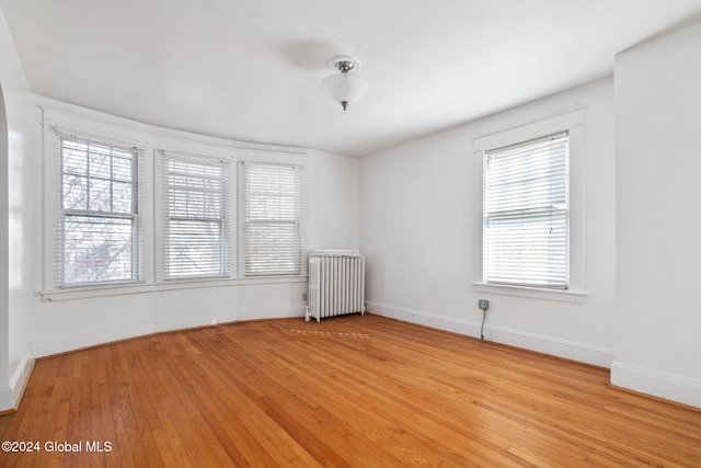 empty room featuring light wood-type flooring, radiator heating unit, and a wealth of natural light