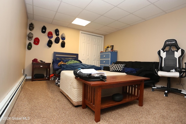 carpeted bedroom with a paneled ceiling, a closet, and a baseboard radiator