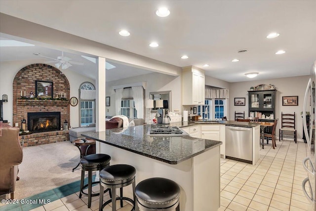 kitchen featuring dark stone counters, ceiling fan, a kitchen bar, kitchen peninsula, and stainless steel appliances