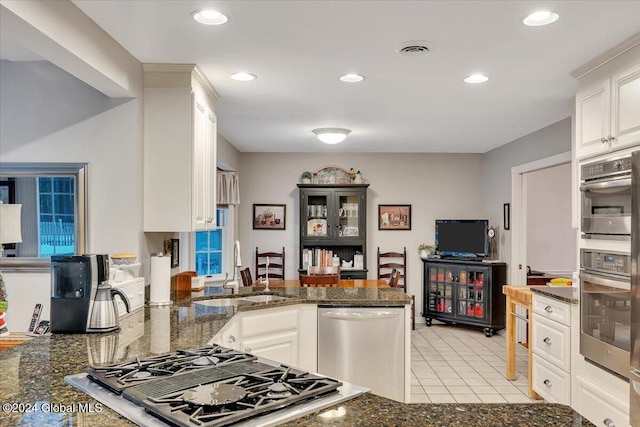 kitchen featuring appliances with stainless steel finishes, sink, dark stone countertops, white cabinets, and light tile patterned flooring