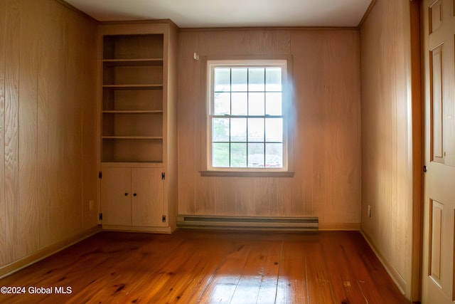 unfurnished room featuring hardwood / wood-style flooring, wood walls, and a baseboard heating unit