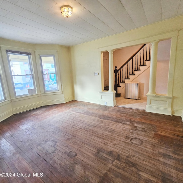 empty room with wood-type flooring, radiator heating unit, and decorative columns