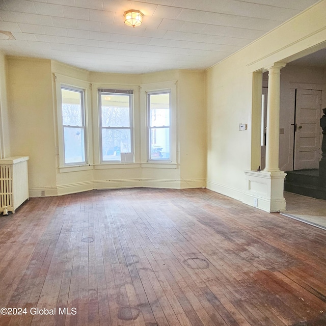 empty room featuring hardwood / wood-style floors, radiator heating unit, and ornate columns