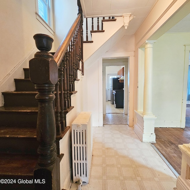 staircase featuring ornate columns, radiator heating unit, and wood-type flooring