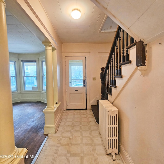 entryway with decorative columns, radiator heating unit, and light wood-type flooring