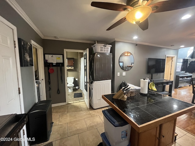 kitchen featuring tile countertops, ceiling fan, ornamental molding, light tile patterned floors, and stacked washer / dryer