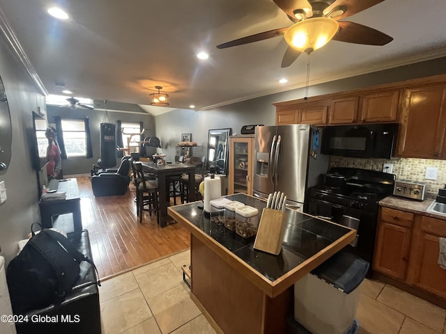 kitchen featuring backsplash, light hardwood / wood-style flooring, ornamental molding, and black appliances