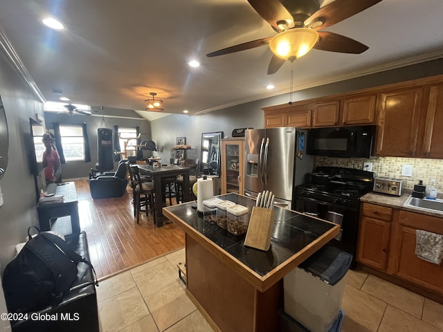 kitchen featuring light wood-type flooring, ornamental molding, sink, black appliances, and a kitchen island