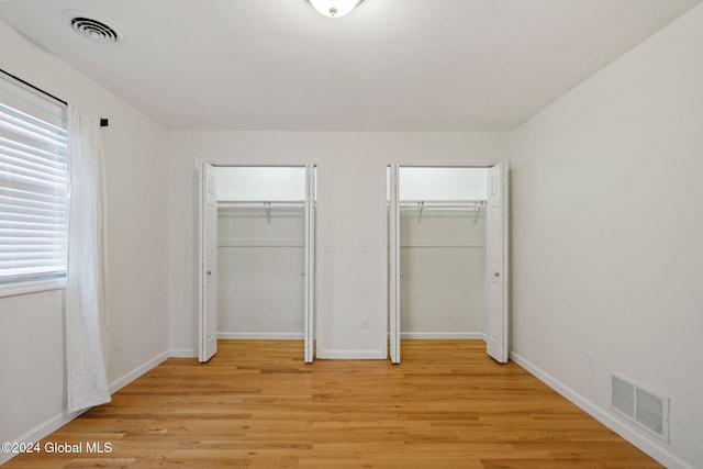 unfurnished bedroom with light hardwood / wood-style floors and multiple closets